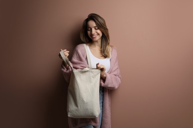 Happy young woman with blank eco friendly bag against light brown background