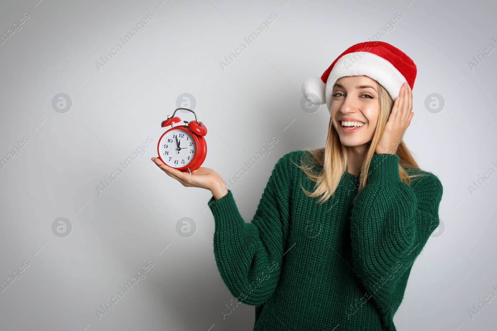Photo of Woman in Santa hat with alarm clock on white background, space for text. New Year countdown