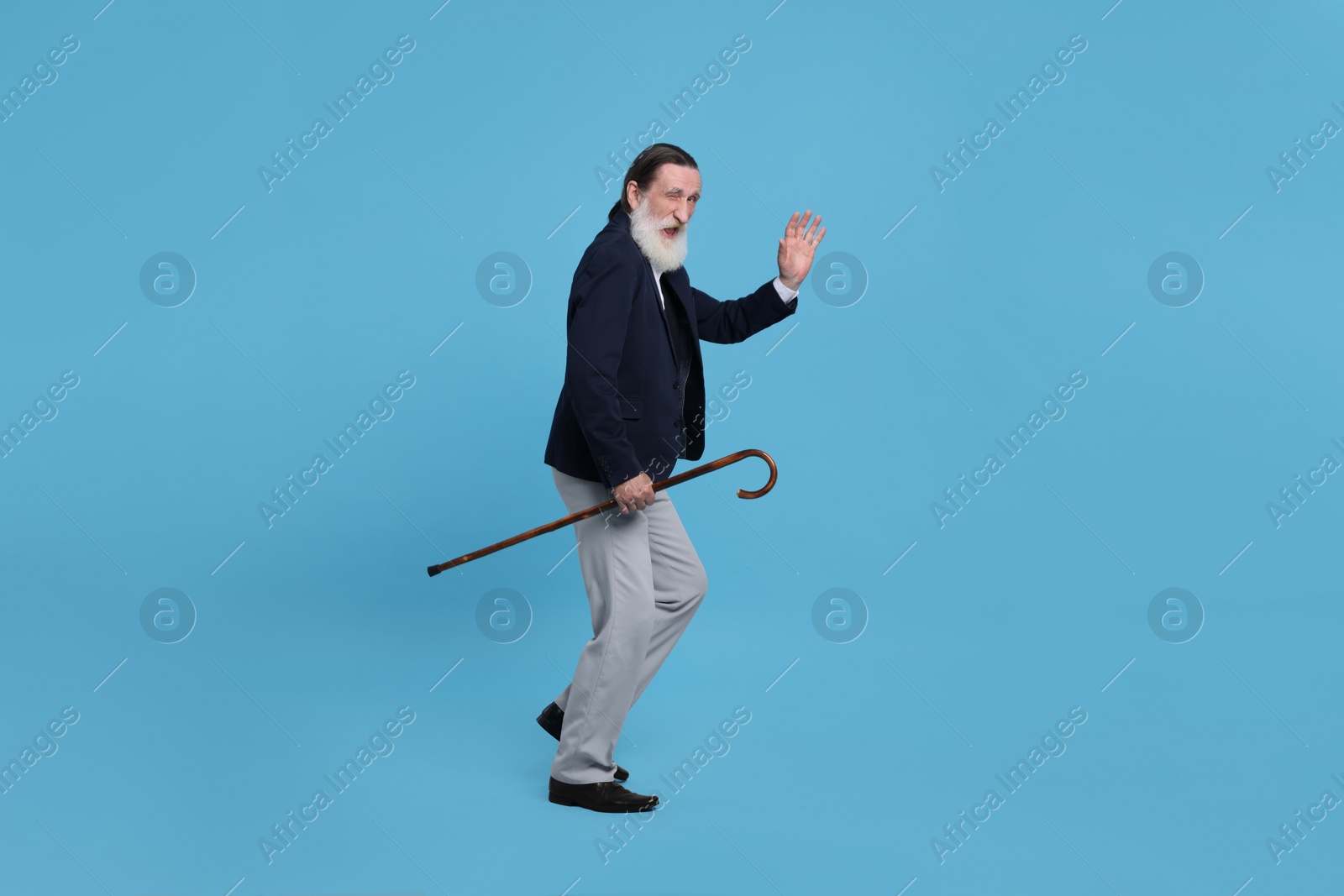 Photo of Senior man with walking cane waving on light blue background