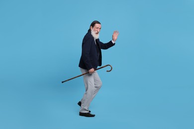 Photo of Senior man with walking cane waving on light blue background