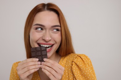 Photo of Young woman eating tasty chocolate on light grey background, space for text