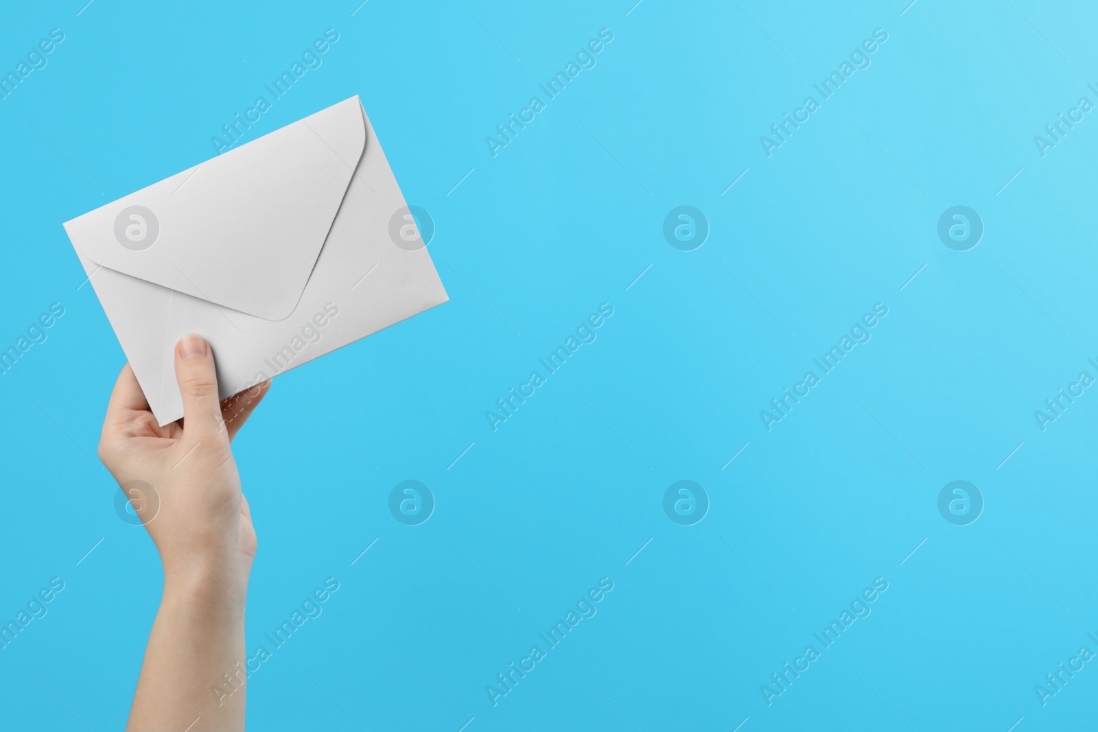 Photo of Woman holding white paper envelope on light blue background, closeup. Space for text