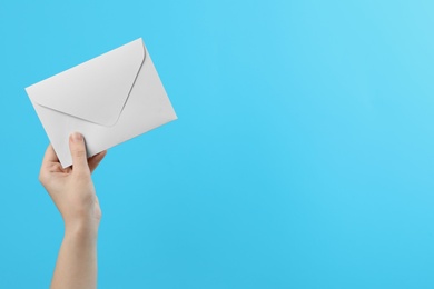 Woman holding white paper envelope on light blue background, closeup. Space for text