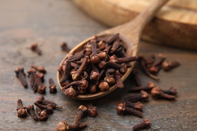 Spoon with aromatic cloves on wooden table, closeup