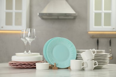 Photo of Clean plates, cups, glasses and bowl on white marble table in kitchen