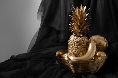 Photo of Golden bowl with fruits on black fabric against light grey background. Space for text