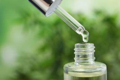 Essential oil dripping from pipette into glass bottle, closeup