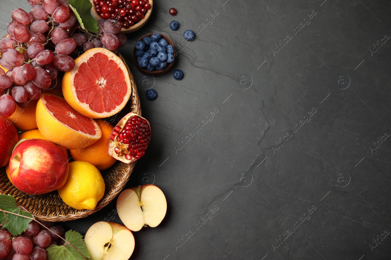 Photo of Wicker basket with different fruits and berries on black table, flat lay. Space for text