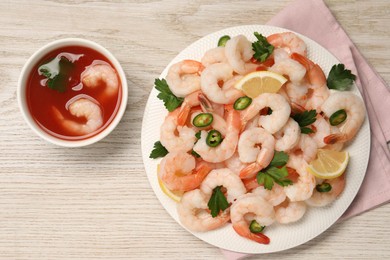 Photo of Tasty boiled shrimps with cocktail sauce, chili, parsley and lemon on light wooden table, flat lay