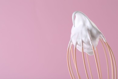 Whisk with whipped cream on pink background, closeup. Space for text