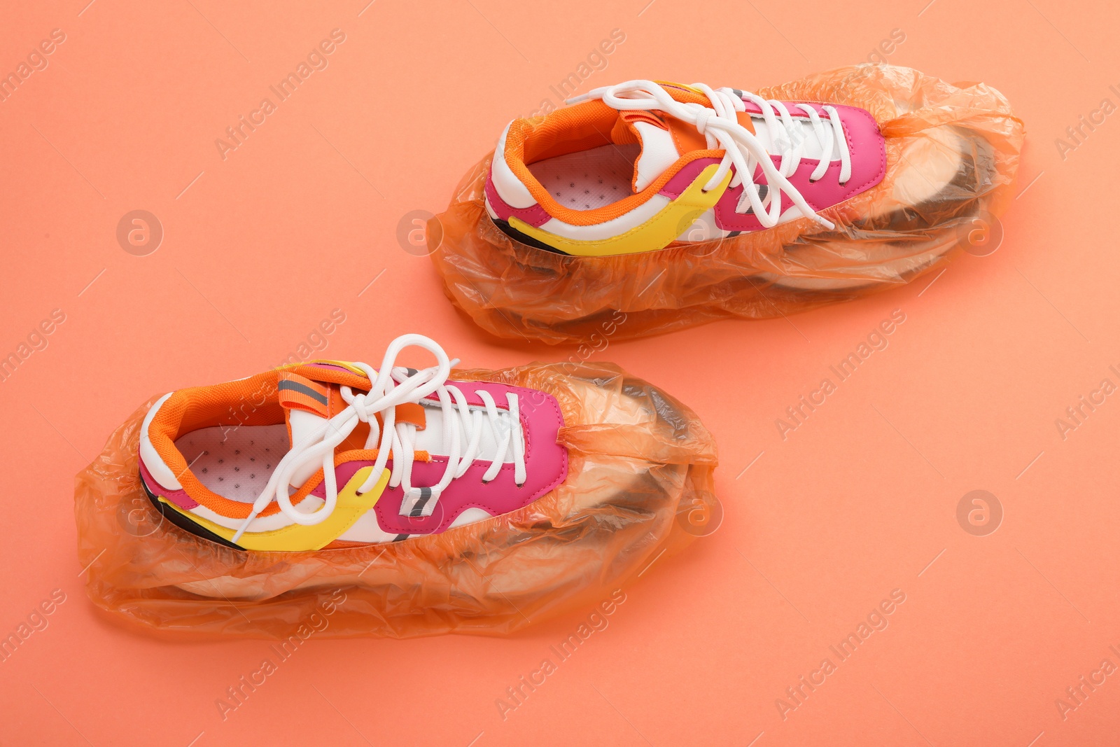 Photo of Women's sneakers in shoe covers on coral background, above view
