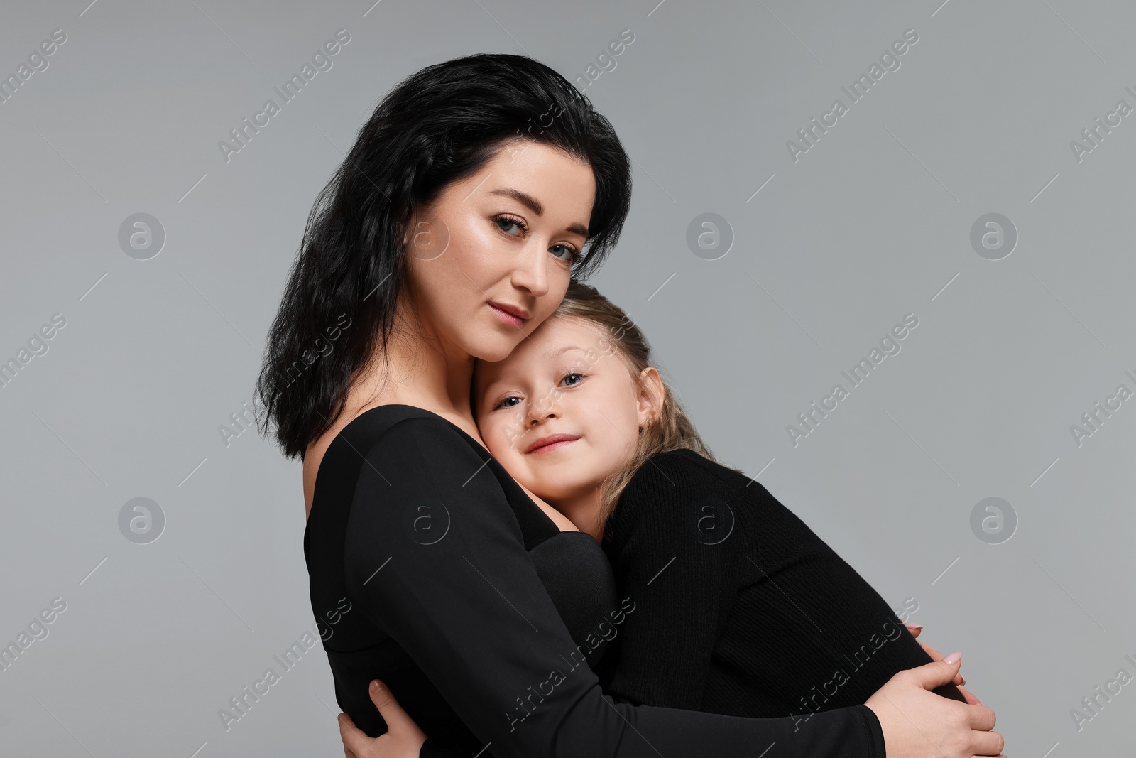 Photo of Beautiful mother hugging with little daughter on grey background