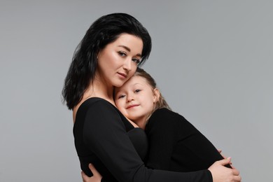 Beautiful mother hugging with little daughter on grey background