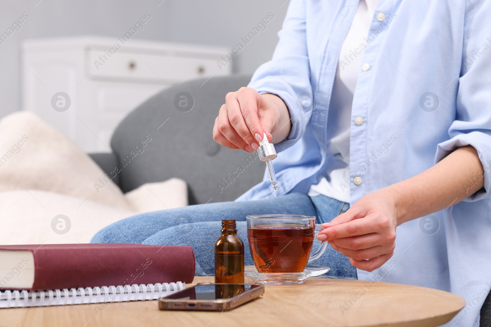 Photo of Woman dripping food supplement into cup of tea at wooden table indoors, closeup