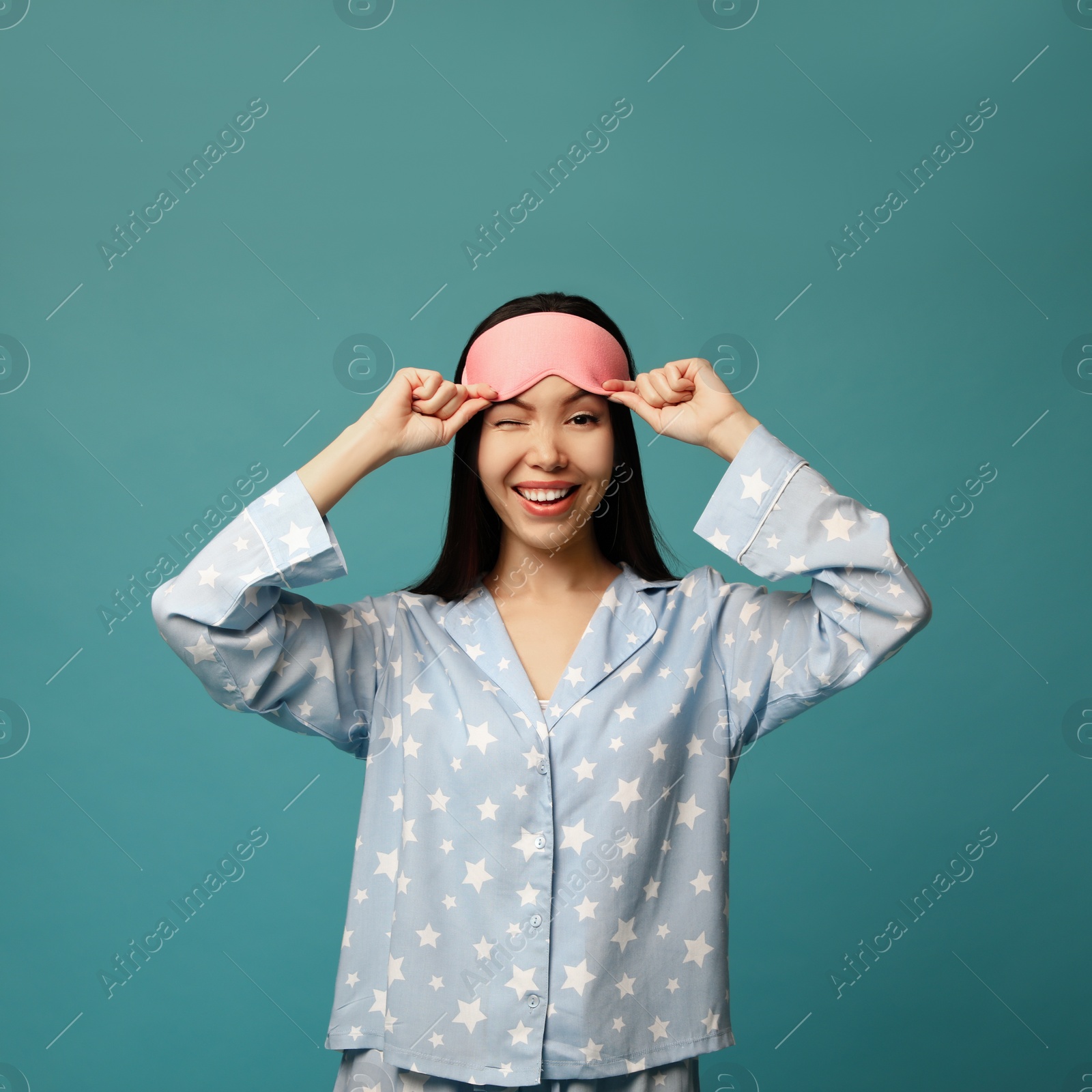 Photo of Beautiful Asian woman wearing pajamas and sleeping mask on blue background. Bedtime