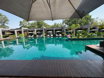 Photo of Swimming pool with wooden deck, exotic plants, umbrellas and sunbeds at luxury resort
