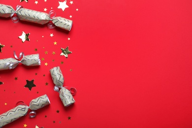 Photo of Open and closed Christmas crackers with shiny confetti on red background, flat lay. Space for text