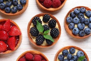 Photo of Tartlets with different fresh berries on white wooden table, flat lay. Delicious dessert