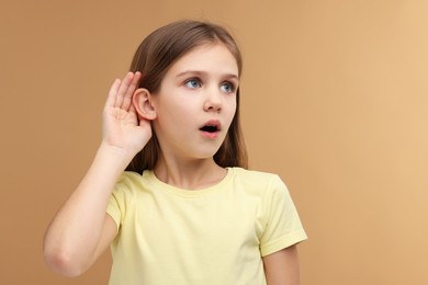 Little girl with hearing problem on pale brown background, space for text