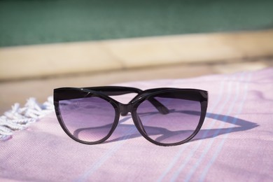 Photo of Stylish sunglasses on blanket near outdoor swimming pool, closeup