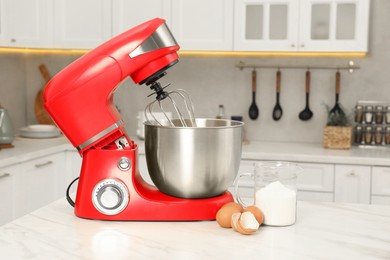 Photo of Modern red stand mixer, eggs and container with flour on white marble table in kitchen