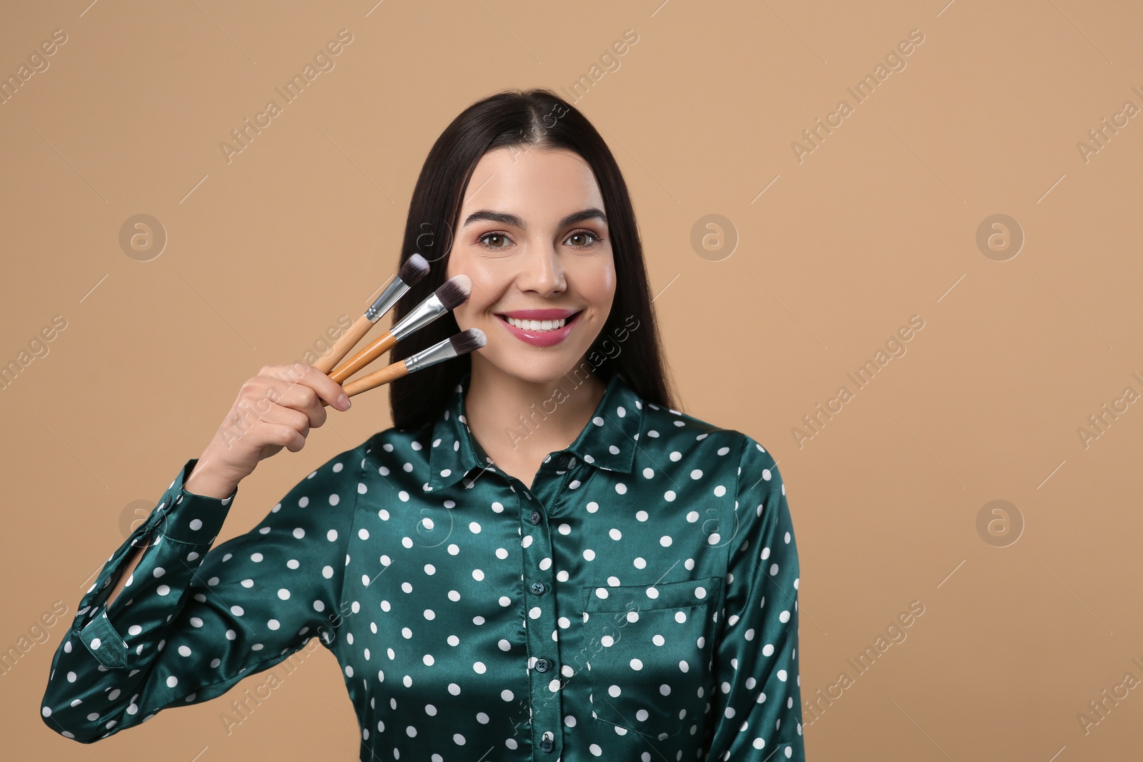 Photo of Happy woman with different makeup brushes on light brown background. Space for text