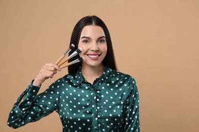 Photo of Happy woman with different makeup brushes on light brown background. Space for text