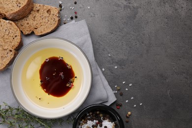 Photo of Bowl of organic balsamic vinegar with oil, spices and bread slices on grey table, flat lay. Space for text