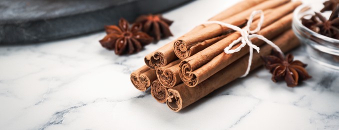 Aromatic cinnamon sticks and anise on white marble table, closeup. Banner design