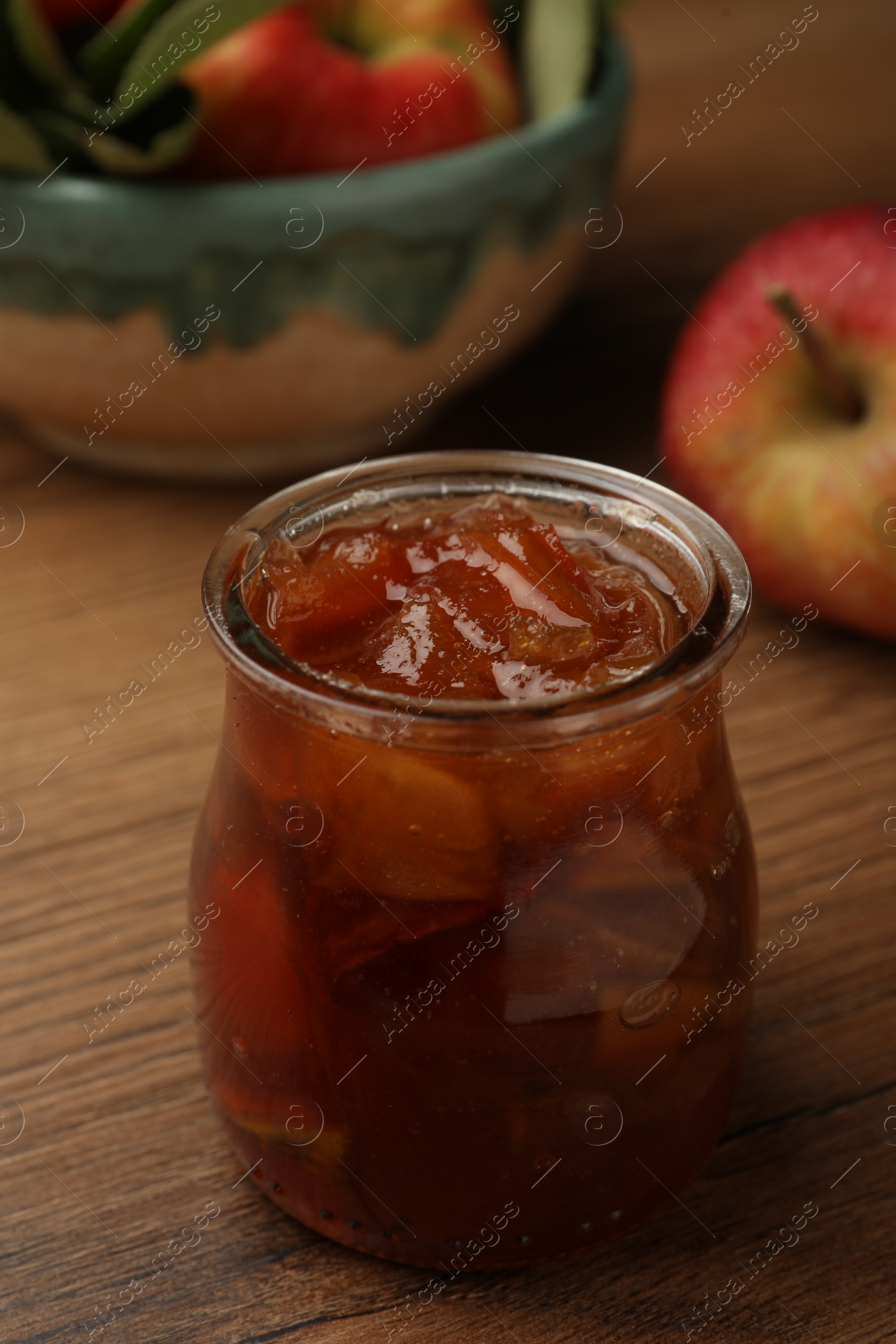 Photo of Tasty apple jam in glass jar on wooden table, closeup