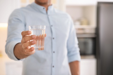 Photo of Man holding glass of pure water in kitchen, closeup