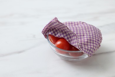 Tomatoes in bowl covered with beeswax food wrap on white table, closeup. Space for text