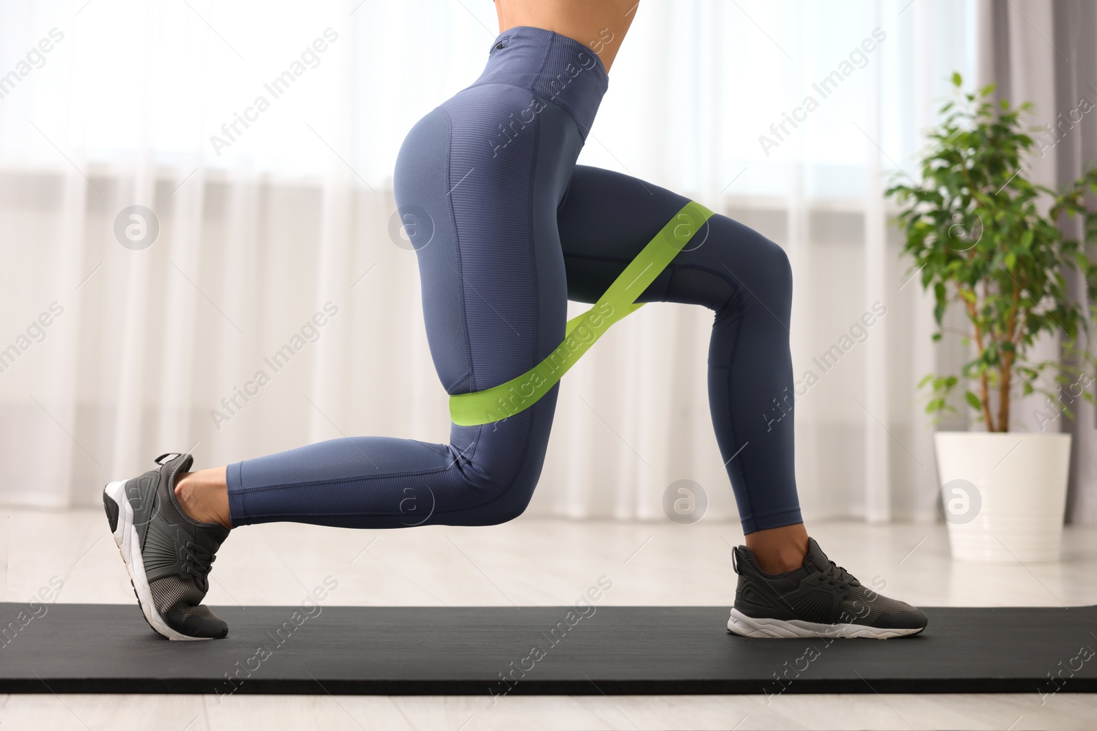 Photo of Woman doing exercise with fitness elastic band on mat indoors, closeup