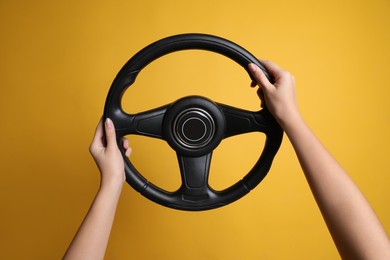 Photo of Woman holding steering wheel on yellow background, closeup