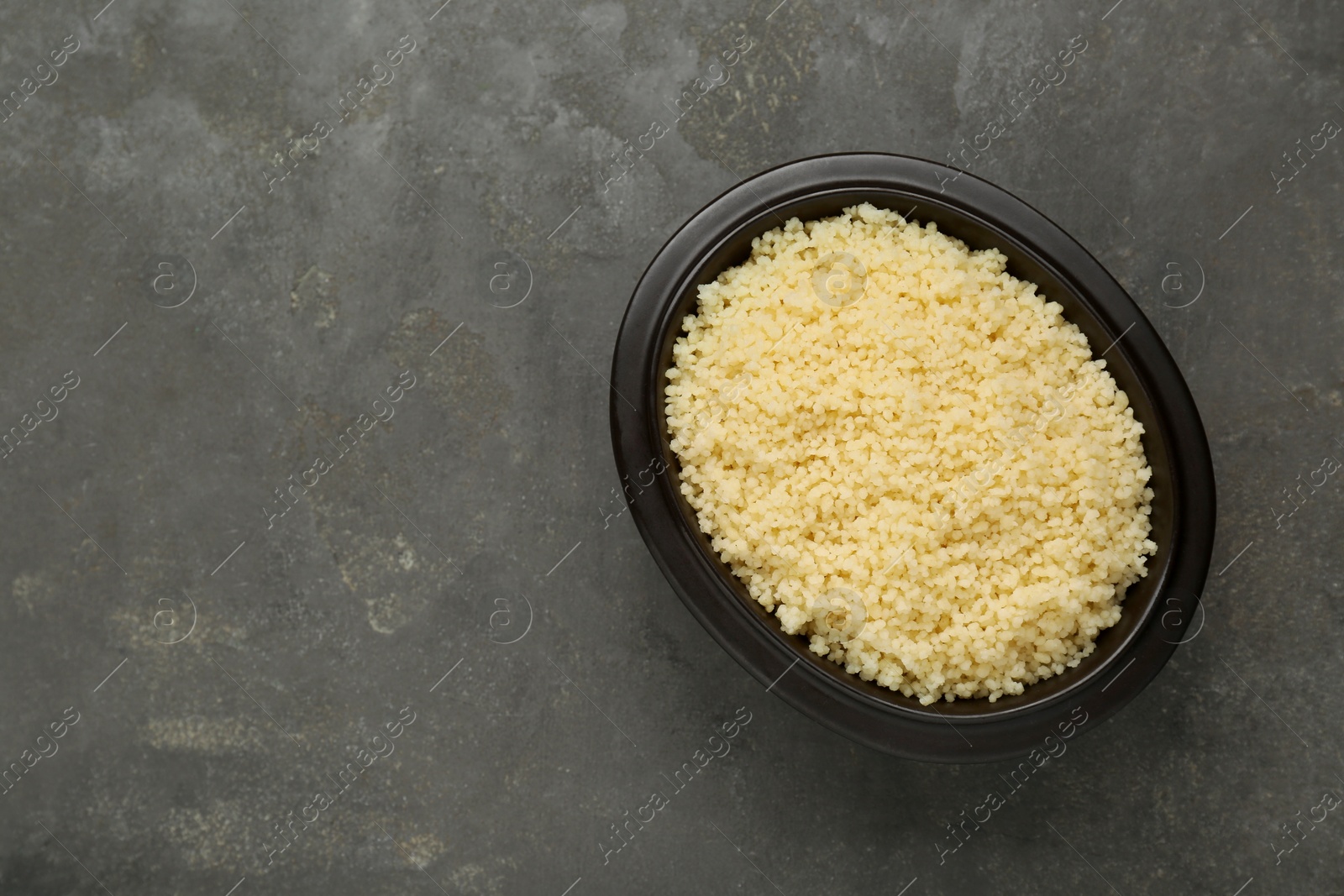 Photo of Bowl of tasty couscous on grey table, top view. Space for text