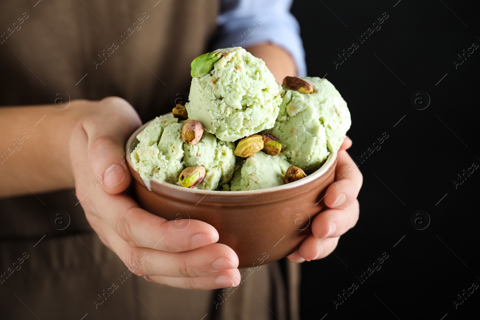 Photo of Woman holding bowl full of pistachio ice cream on black background, closeup. Space for text