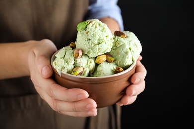 Woman holding bowl full of pistachio ice cream on black background, closeup. Space for text