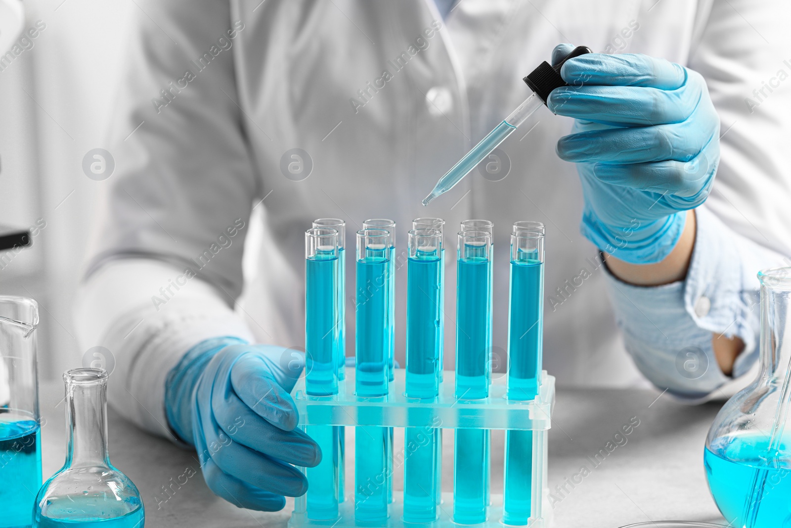 Photo of Scientist dripping liquid from pipette into test tube at white table in laboratory, closeup