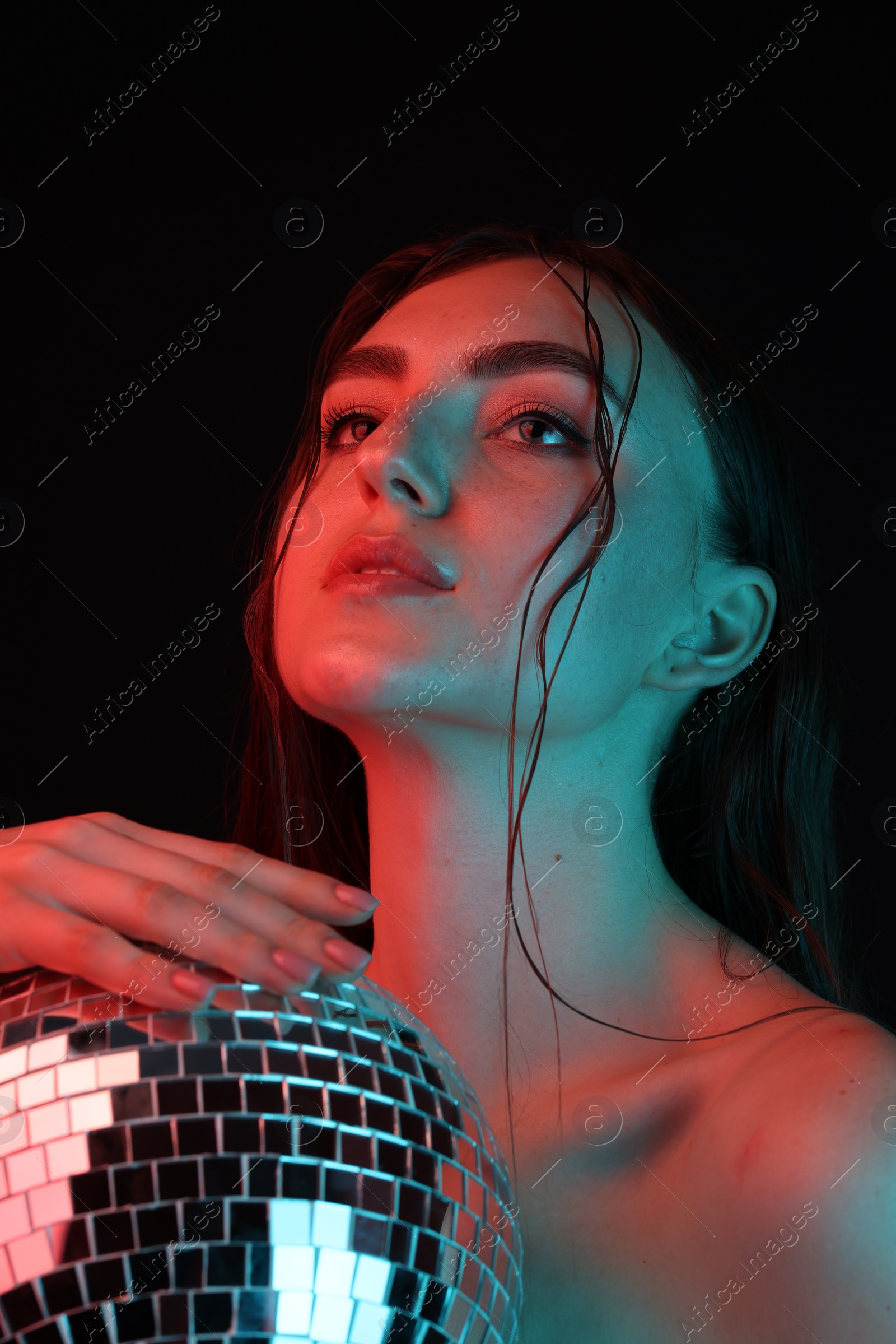 Photo of Beautiful woman with disco ball posing in neon lights against black background