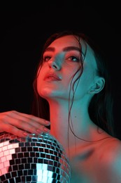 Beautiful woman with disco ball posing in neon lights against black background