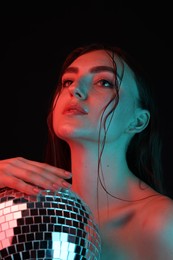 Photo of Beautiful woman with disco ball posing in neon lights against black background