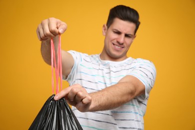 Man holding full garbage bag against yellow background, focus on hands