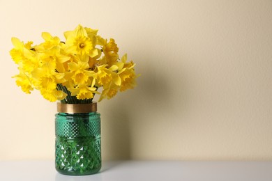 Beautiful daffodils in vase on white table near light wall, space for text