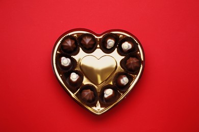 Photo of Heart shaped box with delicious chocolate candies on red background, top view