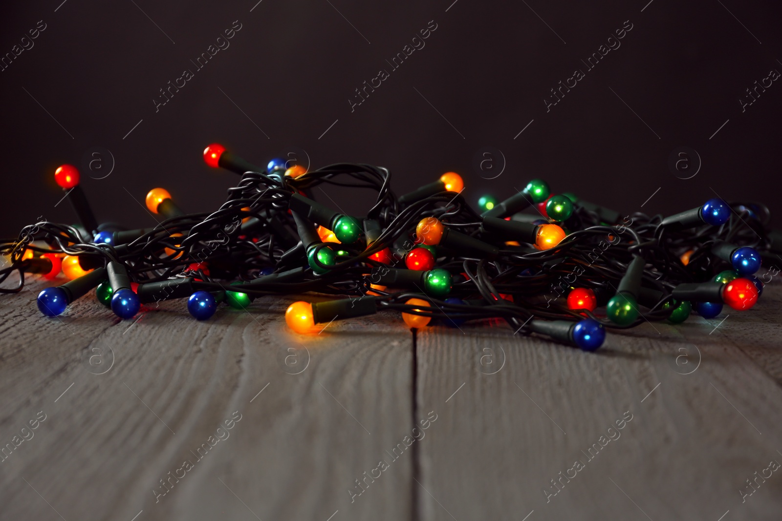 Photo of Beautiful glowing Christmas lights on wooden table against black background