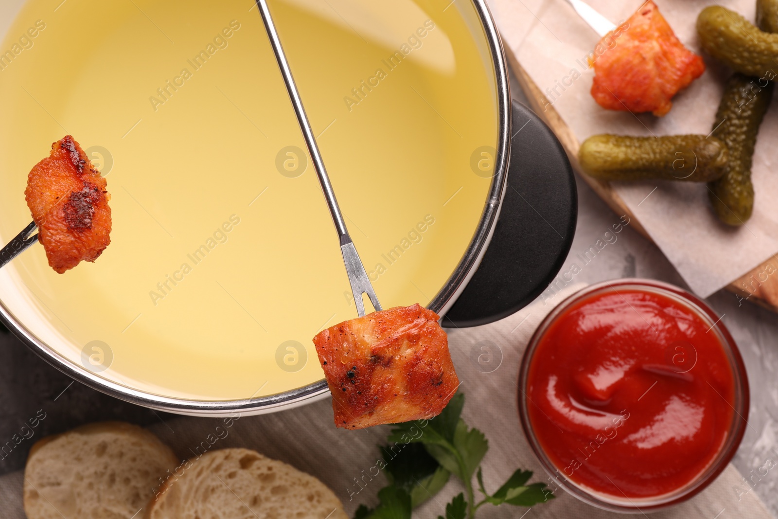 Photo of Fondue pot, forks with fried meat pieces, ketchup and other products on grey textured table, flat lay