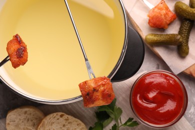 Photo of Fondue pot, forks with fried meat pieces, ketchup and other products on grey textured table, flat lay