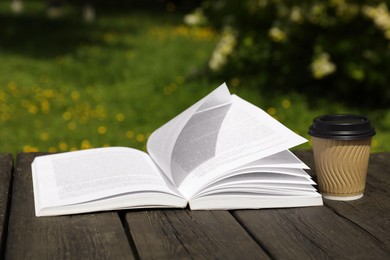 Photo of Open book and paper coffee cup on wooden table outdoors