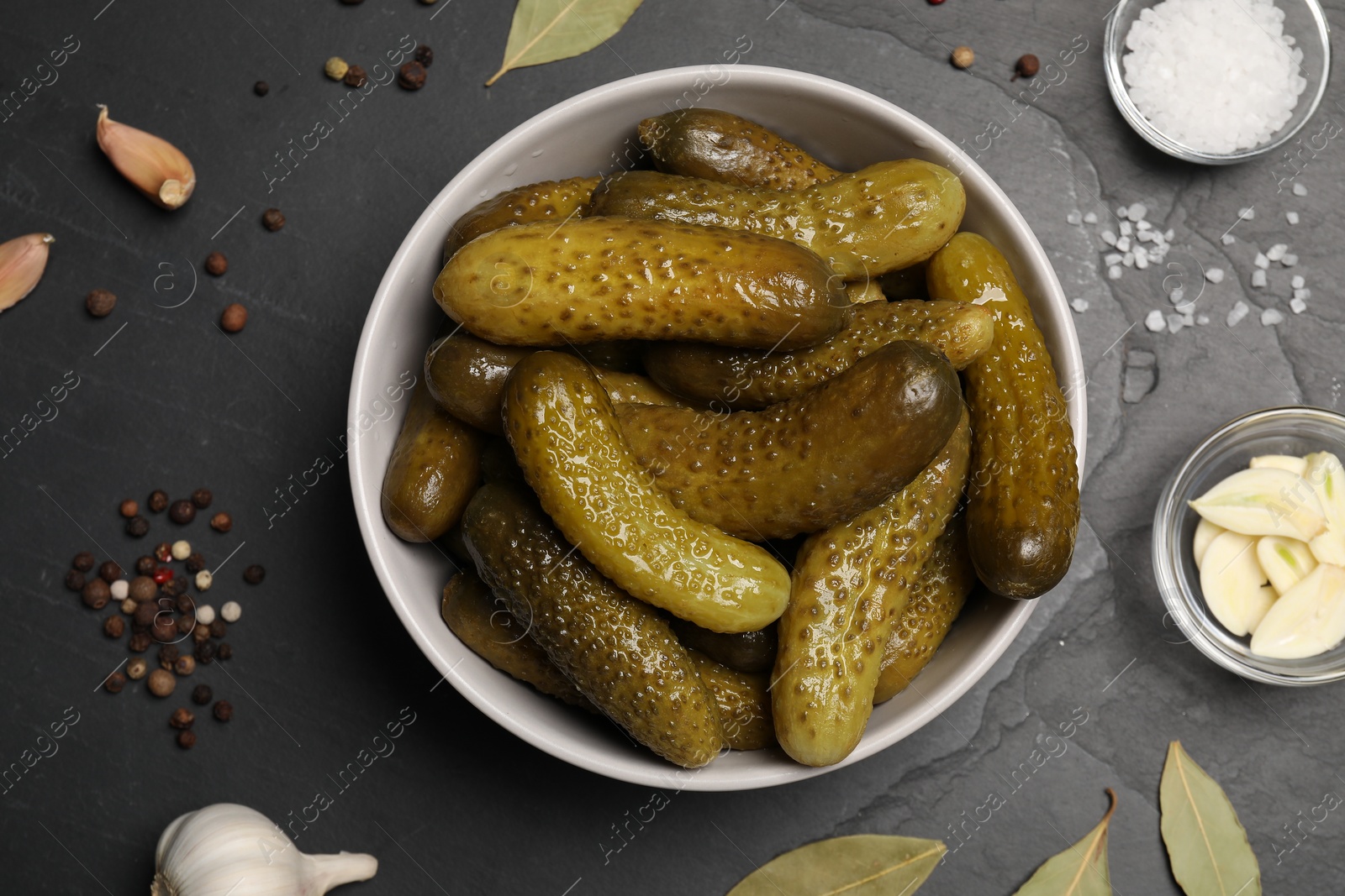 Photo of Tasty pickled cucumbers in bowl and spices on grey table, flat lay