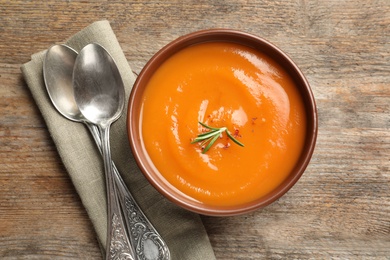 Bowl of tasty sweet potato soup and spoons on wooden table, top view